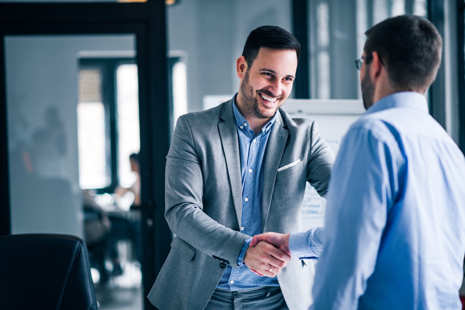 Two male public adjusters in long beach smiling and shaking hands while standing office