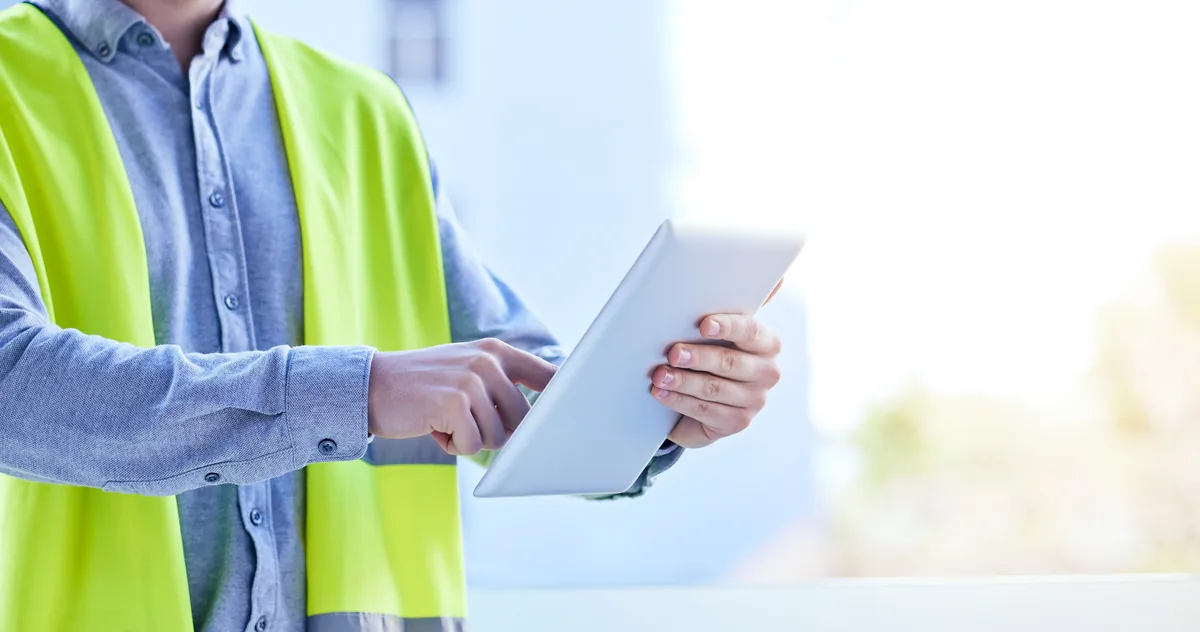 Close-up of a person in a safety vest holding a clipboard and reviewing documents during an inspection.