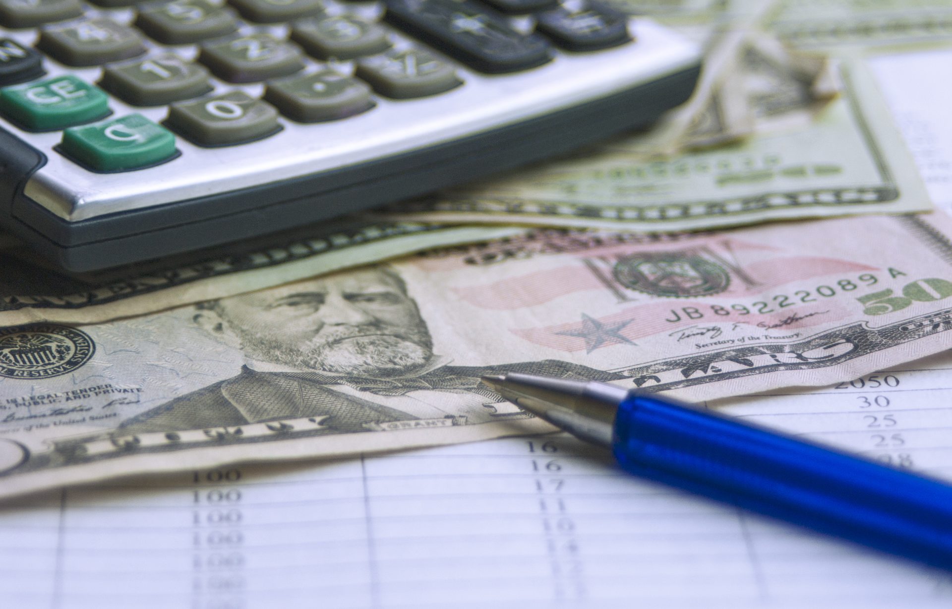 Calculator, cash, and a pen on a ledger, representing calculating an ALE insurance payout